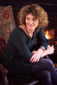 author pic - Lorna Brown - Black outfit red hair in front of a fireplace Review Treading the Uneven Road