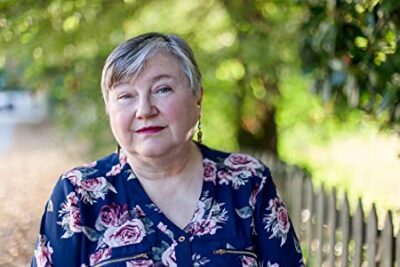 As Long As You're Mine by Jenna Jaxon | Historical Romance Review 2 Jenna Jaxon, author image, facing the camera, wearing a blue floral print top with a blurred outdoor background