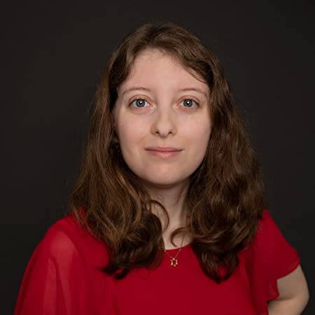 Elyse Hoffman Author Profile Image with wavy shoulder-length brown hair and wearing a red top, looking straight at camera against a dark background.