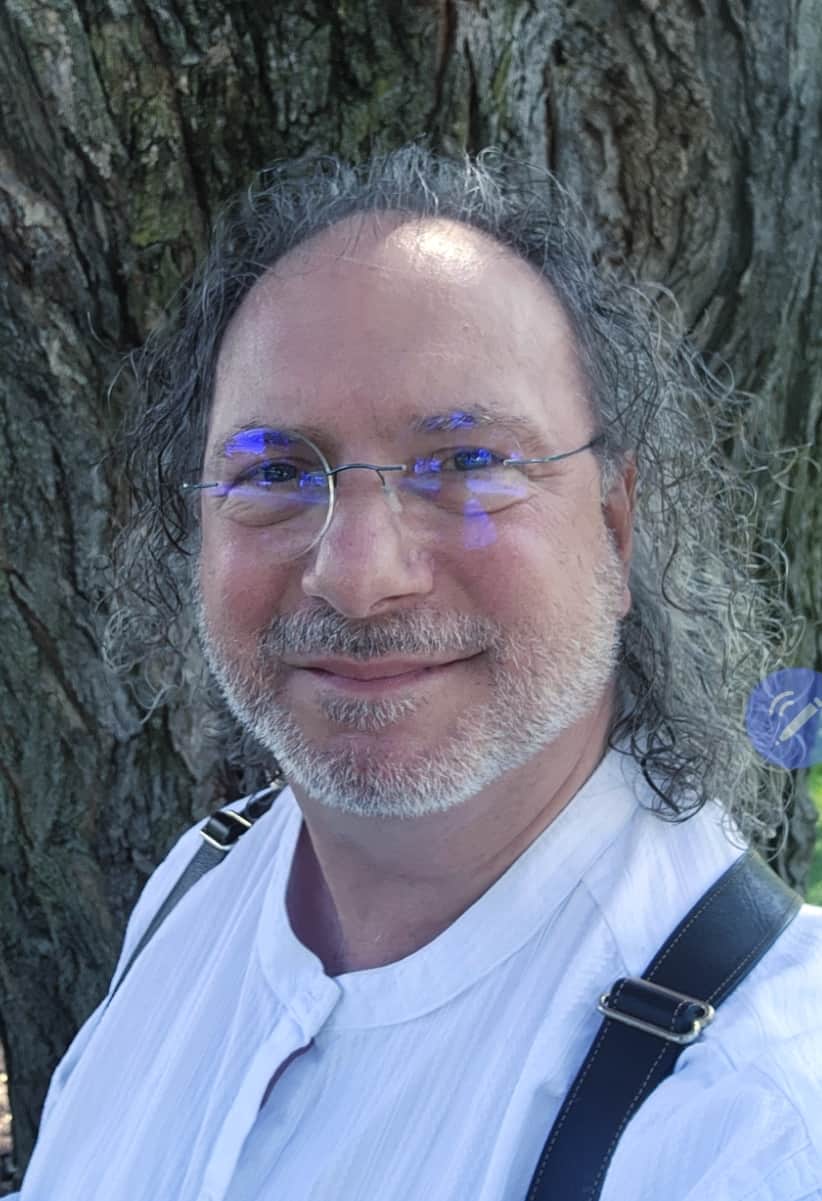 Frederick J. Burns, author of And The Trees Talked Back, smiling in front of a large tree trunk.