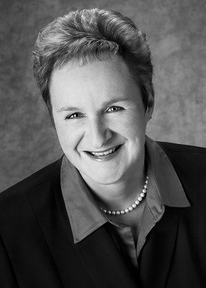 Black-and-white professional headshot of Annette Oppenlander, author of “Coal Dreams.” She is smiling, wearing a blazer and pearl necklace, with a neutral studio background.