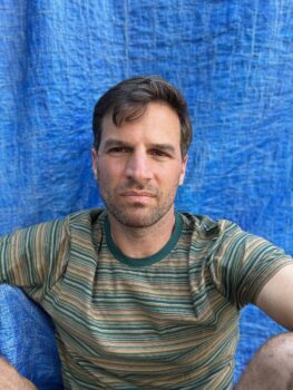 Philip Reari Author Profie image Blue background, green shirt, stoic face