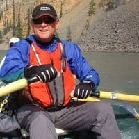 Jim McAllister Author Profile image - author in a blue jacket rowing a boat on a lake