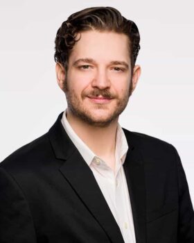Allen Lyle, author of Red Sun Rising, wearing a black suit jacket and white shirt, with a short beard and an enigmatic smile.