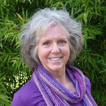 Amanda Iles Author Profile image, head-shoulders, purple blouse, leafy background