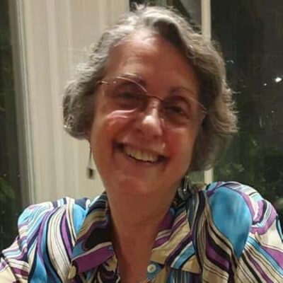 Smiling portrait of M.G. da Mota, author of Stars Maintain Their Glow, wearing glasses and a striped colorful blouse.