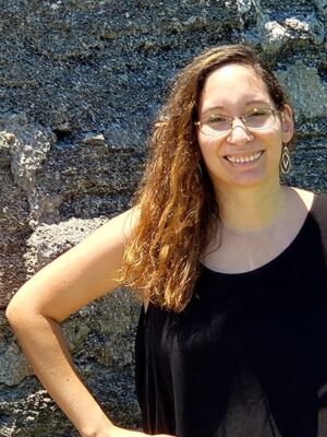 Between the Living and the Dead by Sophie Jupillat Posey – YA Paranormal Mystery Spotlight 6 Author posing in from of rocks. black top brown hair, glasses