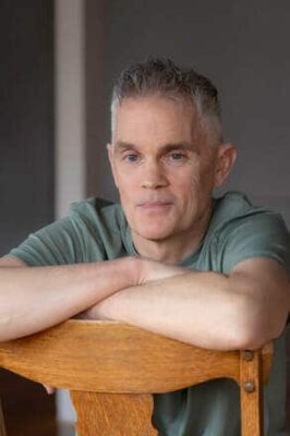 Daniel Chambrello author image leaning on the back of a chair with arms crossed