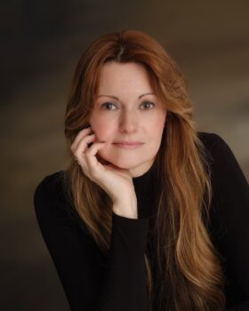 Avery Sterly author profile imagelight brown background with author in dark sweater and red hair