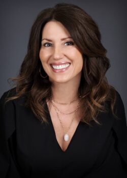 The Price of Truth, A Chasing Peace Novel, by Michele Clarizio 7 Author Michele Clarizio smiling in front of a neutral gray background. She has long dark brown hair, wears a black top with a gold necklace, and projects warmth and confidence.