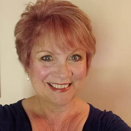 Author photo of C.S. McDonald. She is smiling and seated in a warm indoor setting, wearing a black top with a friendly and approachable expression. Best known for her cozy mystery series including Fiona Quinn Mysteries and Owl’s Nest Mysteries.