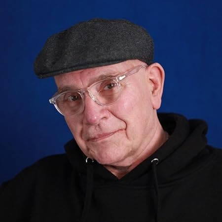 Author L.J. Ambrosio, writer of the Reflections of Michael series, wearing a dark flat cap and black hoodie, against a blue backdrop.