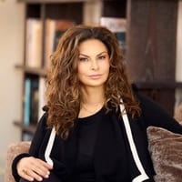 Author Nabila Khashoggi – Mediterranean-born, Europe-raised entrepreneur and cookbook author, seated indoors with bookshelves in the background.