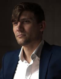 Portrait of author Stuart Heinrich wearing a dark blue blazer and white shirt, softly lit against a neutral background