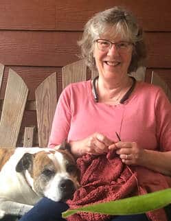 Photo of author M.F. Jones smiling on a porch while knitting, with her rescue dog resting beside her. Casual candid image for the Stones River iRead Book Tours feature