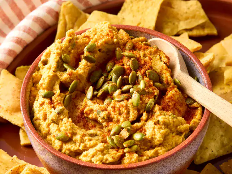 SAvory Pumpkin Hummus with pumpkin seeds on top in a red bowl with pita chips
