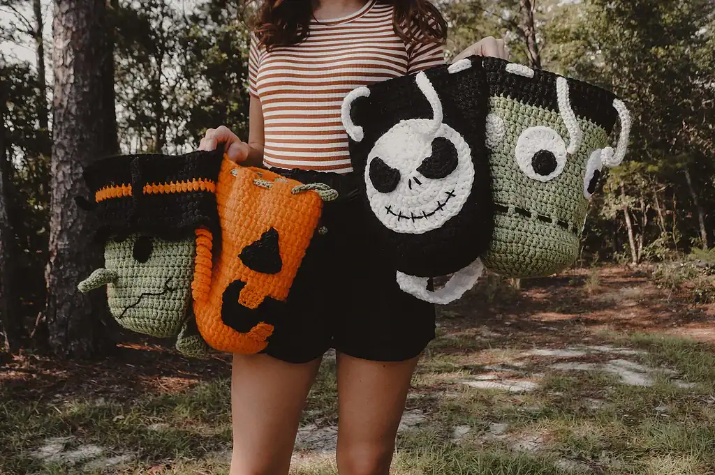Woman in black shorts and orange/white striped shirt holding 4 crocheted halloween treat bags