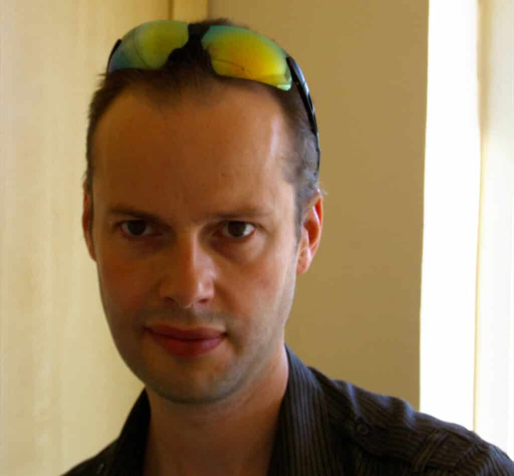 Author photo of Stephen D. Owen, writer of ICENI: The Year of Sacrifice (Book One). He appears indoors wearing a dark shirt and sunglasses resting on his head, looking toward the camera.