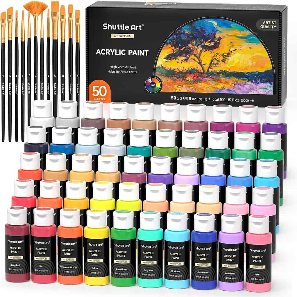 Shuttle Art acrylic paint set with 50 vibrant colors in small bottles, arranged in neat rows beside a set of 12 golden-handled paintbrushes. The black box features a bright landscape painting, emphasizing high-viscosity artist-quality paints perfect for crafts and art projects.
