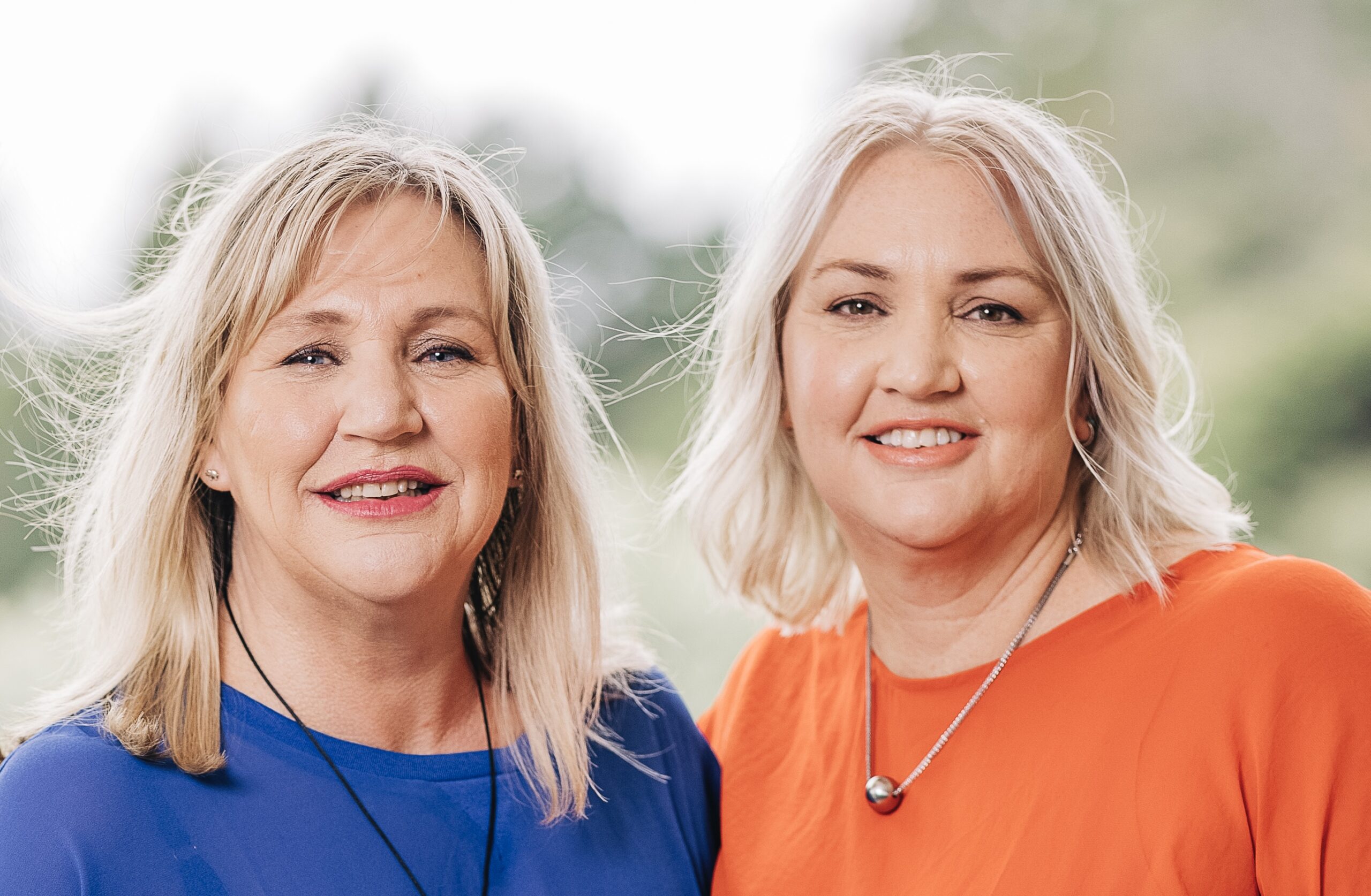 Mary and Bright by Nikki Perry and Kirsty Roby | BBNYA 2025 Semi-Finalist Spotlight 6 Author photo of sister writing duo Nikki Perry and Kirsty Roby. Both women are smiling at the camera outdoors with soft greenery in the background-one wearing a royal-blue top, the other an orange top. Promotional image for their novel Mary and Bright.