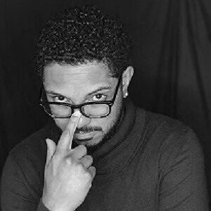 Black and white author photo of Brian Coggins Jr., wearing glasses and looking thoughtfully at the camera, used as the author profile image for "The Olympus Trinity" & future The Worlds of Complexity reviewsbook review on ginaraemitchell.com.