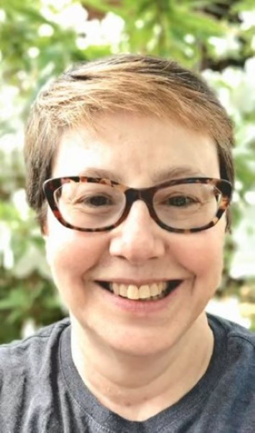 Headshot of author M. Jayne LaDow smiling outdoors with glasses and short light brown hair.