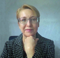 Author portrait of Anne E. Beall, PhD, award-winning author and social psychologist. She is seated indoors, wearing glasses and a patterned jacket, resting her chin on her hand, and smiling gently at the camera against a neutral background.