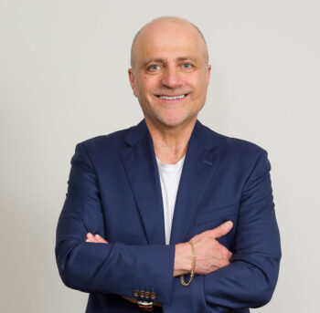 Joseph Gulesserian author image - with folded arms, navy blue suit, facing camera with a smile