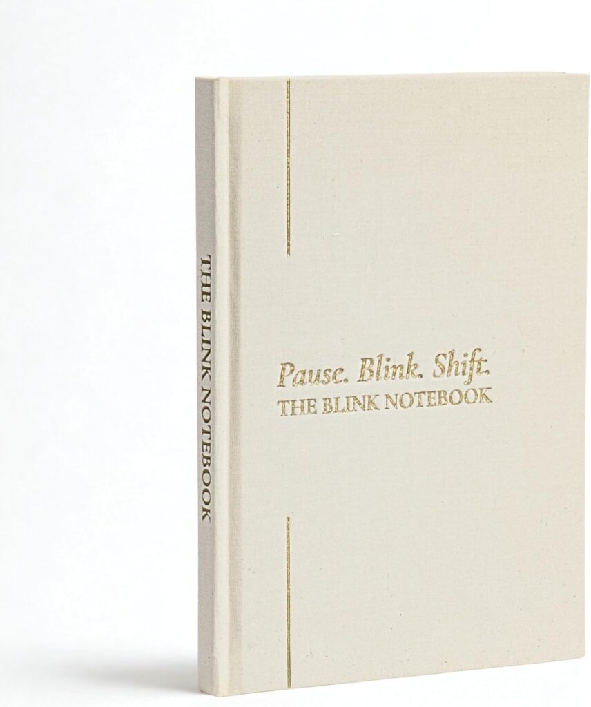 Minimalist hardcover journal titled Pause. Blink. Shift. The Blink Notebook. Features a cream-colored cover with subtle gold embossed text and thin gold vertical lines, photographed against a white background.