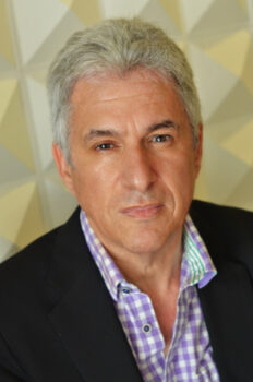 Author portrait of Clive Fleury, showing a gray-haired man wearing a dark jacket and patterned shirt, photographed against a softly lit geometric background.
