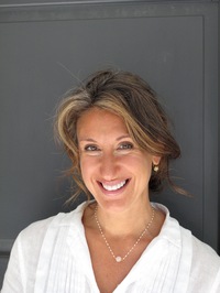 Author photo of Jane Green smiling, wearing a white blouse and gold jewelry against a dark background