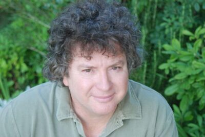 Author photo of Scott Douglas Gerber outdoors against a green natural background, used in connection with the novel The Trafficker on GinaRaeMitchell.com.