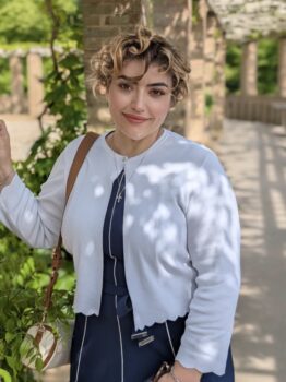 Author photo of S. Jeyran Main standing outdoors along a garden walkway wearing a white cardigan and navy dress.