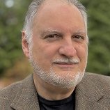 Author photo of Michael Albrego wearing a tan suit & dark shirt, in an outdoor setting.