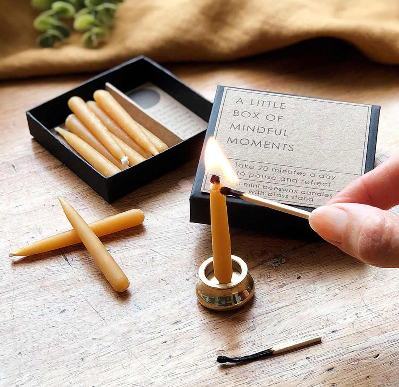 Small beeswax candle set with brass holder, lit on a wooden surface creating a warm, calming atmosphere