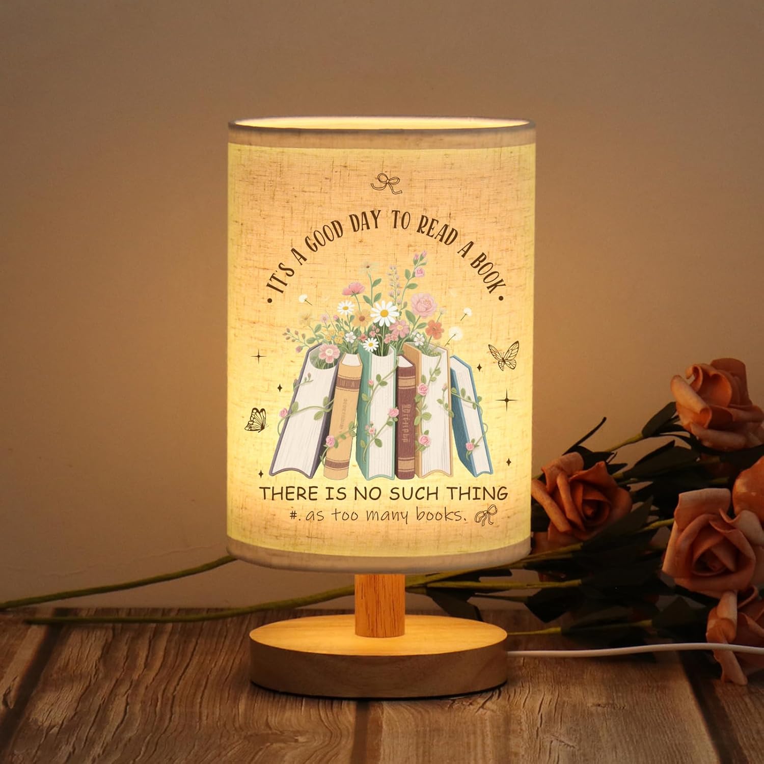 Warm glowing table lamp with a book-themed design and floral illustration, featuring the phrase It's a good day to read a book, on a wooden base.