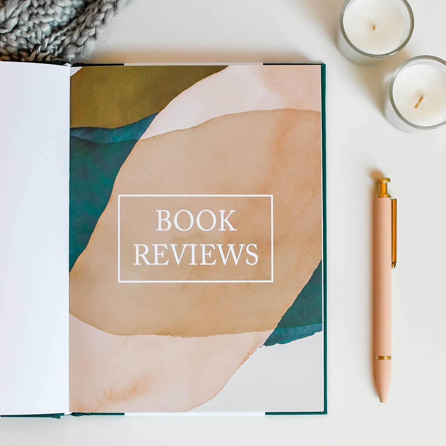 Emerald green reading journal open to a book review page with pen and candles on a soft, neutral background