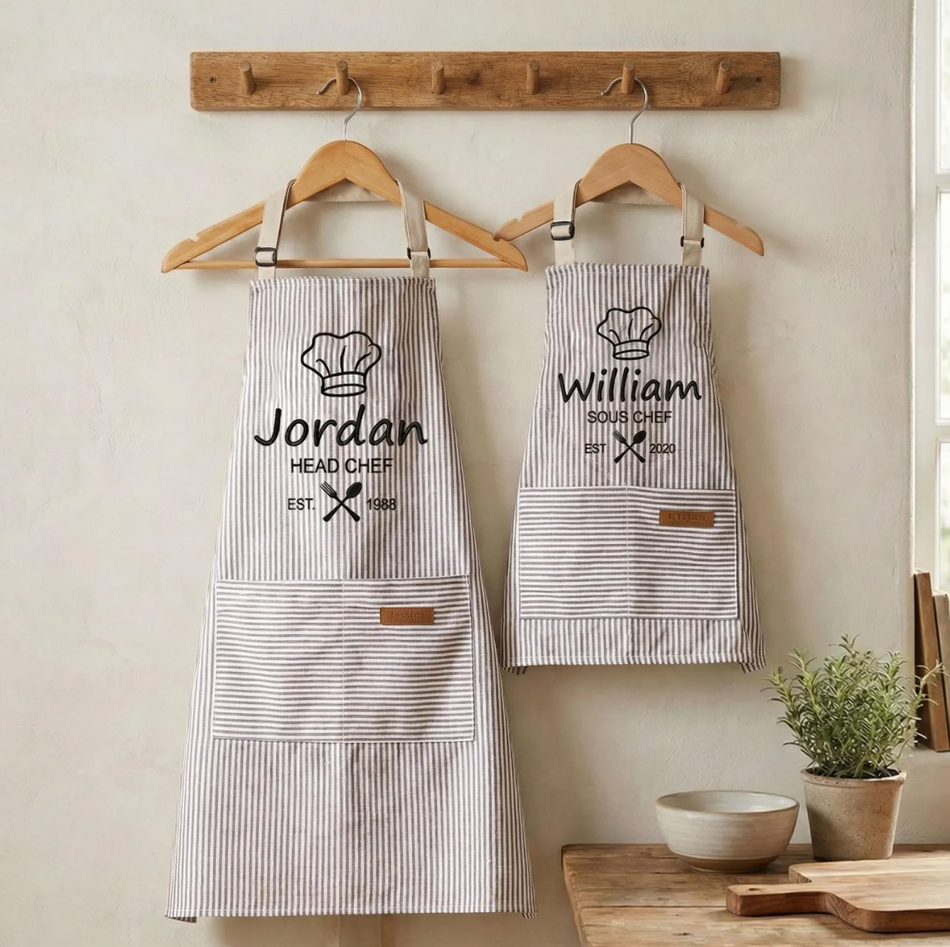 Personalized apron set with Head Chef and Sous Chef text hanging on wooden hooks