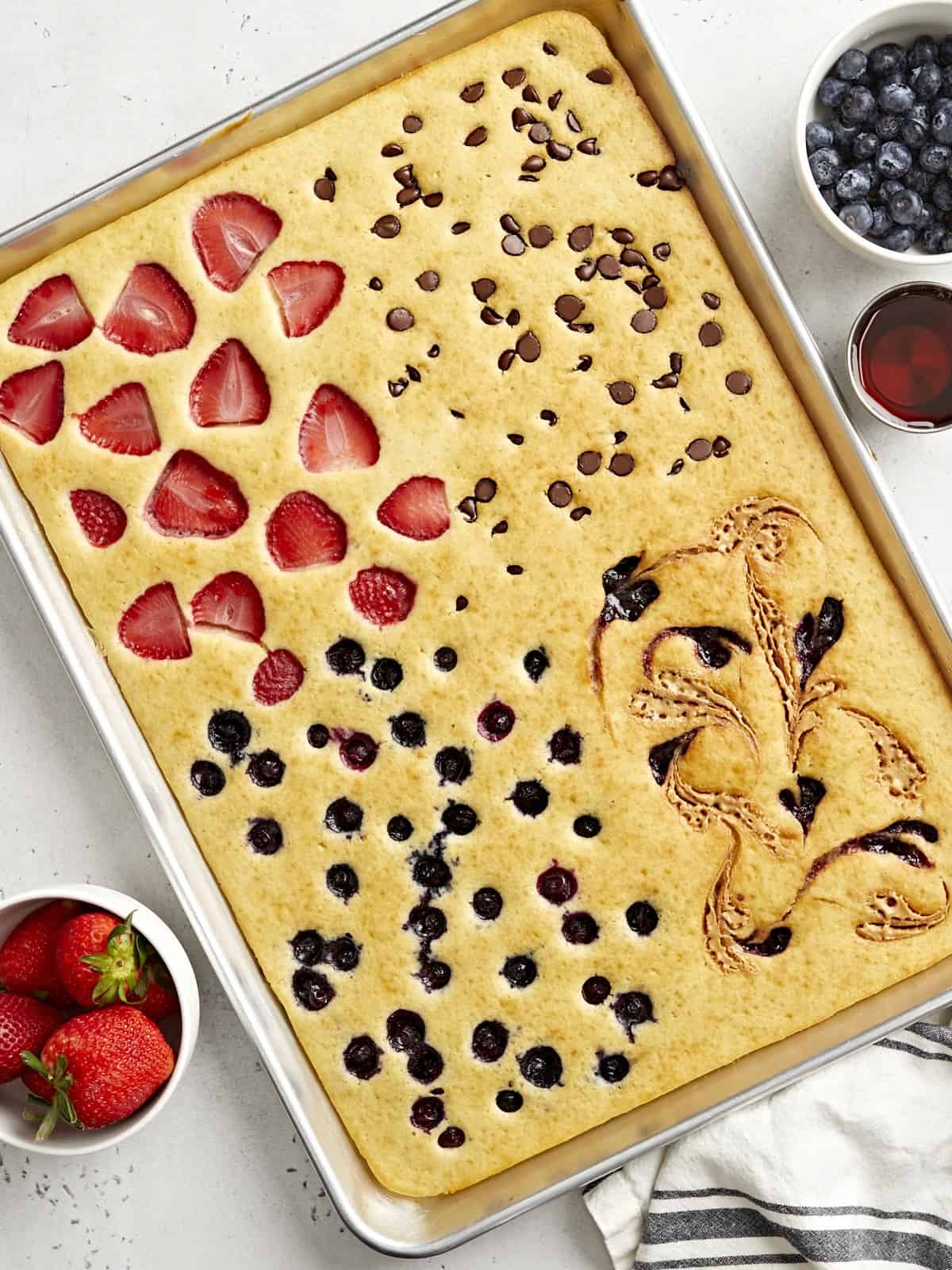 Sheet pan pancakes baked in sections with strawberries, blueberries, and chocolate chips for an easy customizable family breakfast
