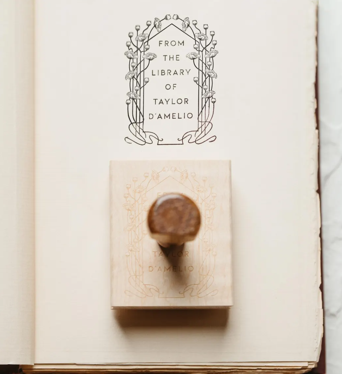 Personalized floral Ex Libris book stamp resting on an open book, showing a delicate Art Deco design.