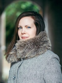 The Eternal Return of Clara Hart by Louise Finch | A Haunting YA Story of Identity and Memory 2 Author photo of Louise Finch wearing a gray coat with a fur collar while standing outdoors near stone arches.
