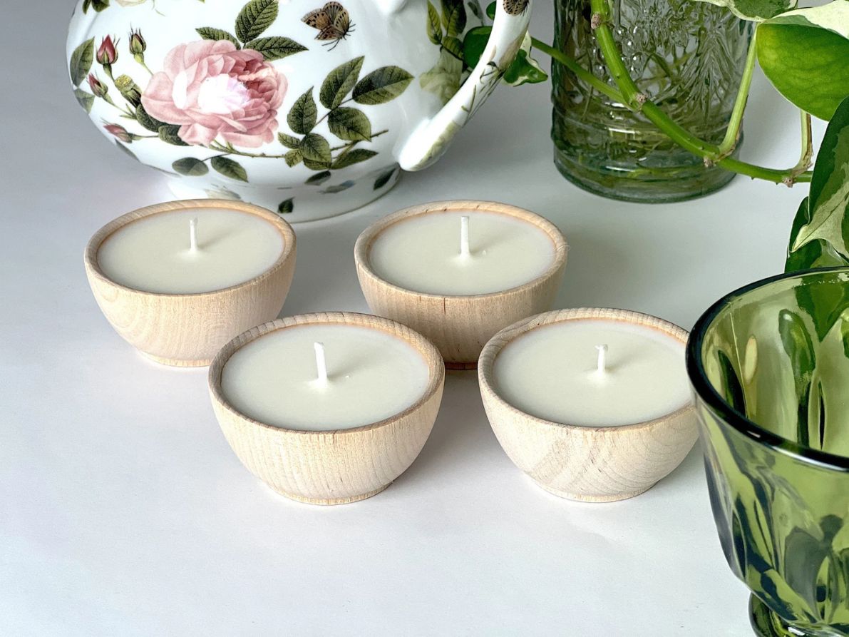 Small natural wood citronella candles arranged on a table beside flowers and greenery.
