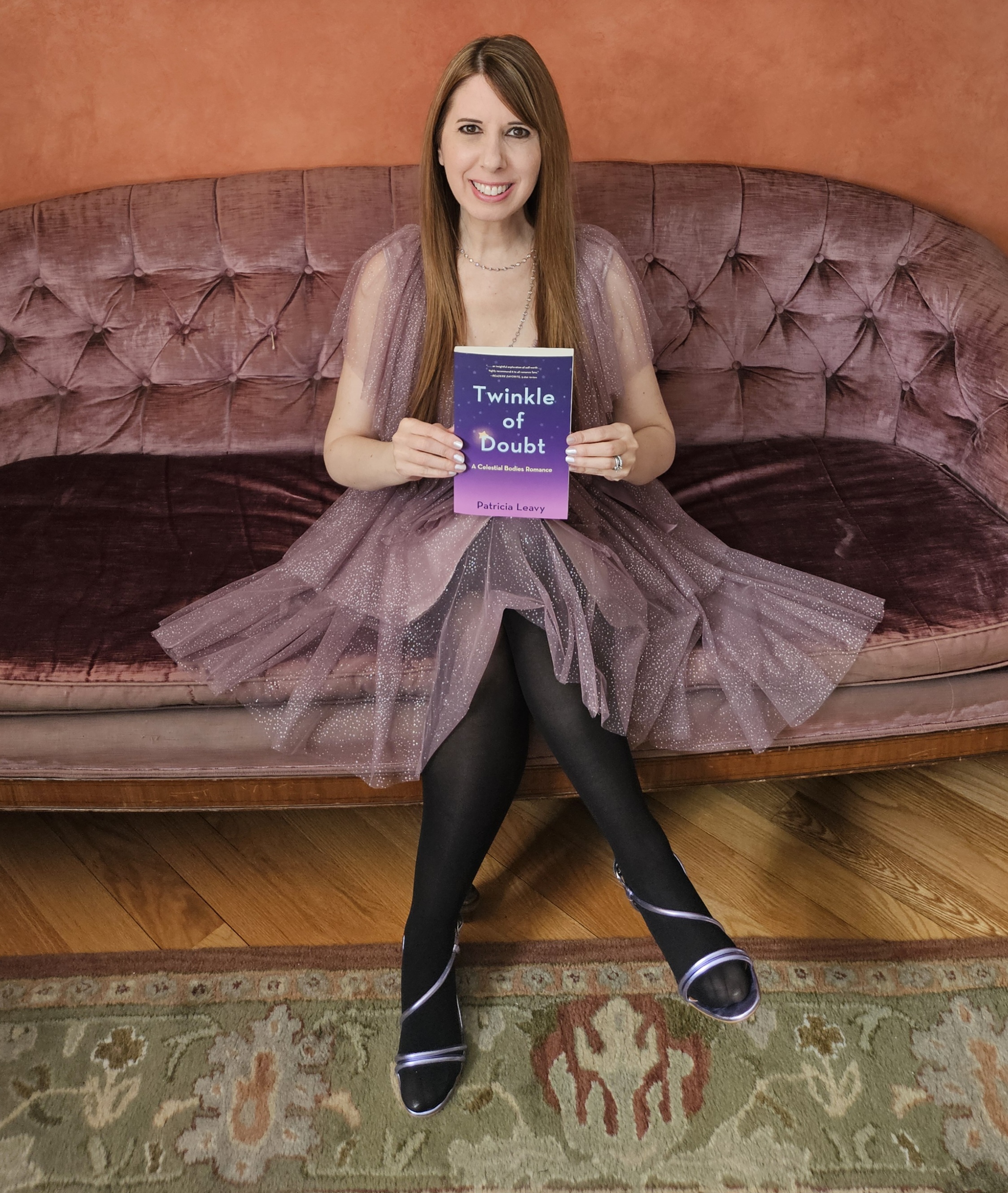  author photo of Patricia Leavy smiling with long straight hair in a mauve chiffon dress seated on a matching sofa.