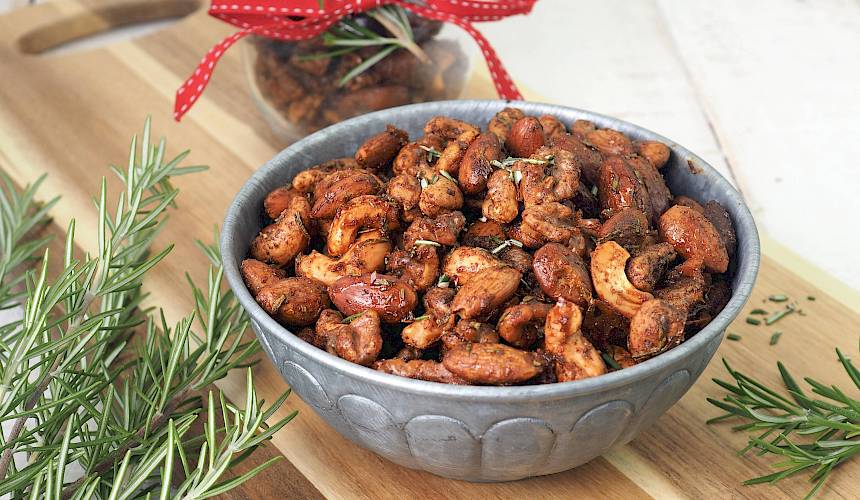 Bowl of rosemary roasted mixed nuts with warm savory seasoning and fresh rosemary sprigs.