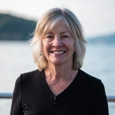 Gail Ward Olmsted Author Profile image 2025 - Author smiling full face, black top, blurred lake background