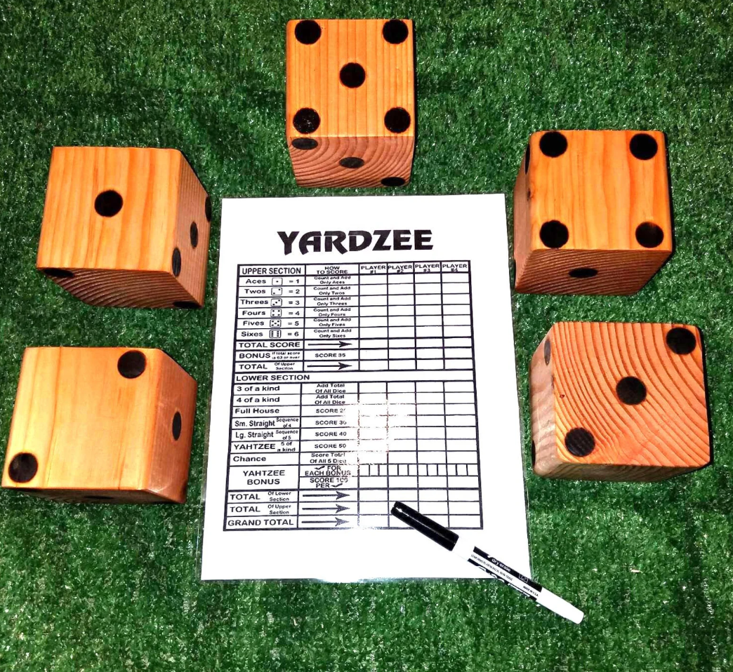 A giant wooden Yardzee game set with oversized dice, scorecard, and marker arranged on green grass for outdoor family play.