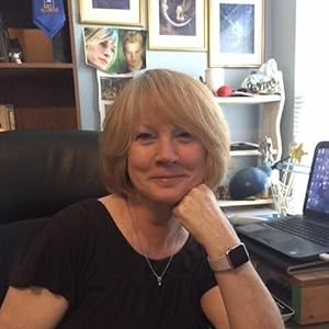 Move Me by Lynn Crandall | A Paranormal Romance of Redemption, Danger & Second Chances 2 Author Lynn Crandall is seated at her desk, smiling with her chin resting on her fist.