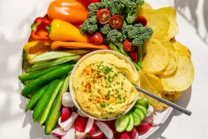 A bowl of deviled egg dip surrounded by vegetables and chips.