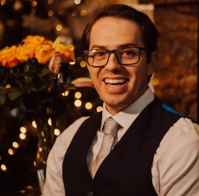 The Below by Scott T. Miller | A Gripping Cyberpunk Thriller Review 2 Author Scott T. Miller smiling while seated indoors wearing glasses, a white shirt, tie, and dark vest.