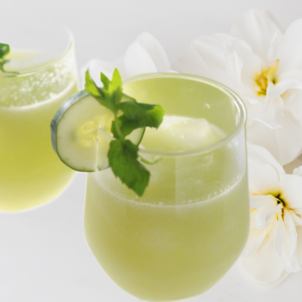 Two glasses of cucumber mint lemonade on a table with white and yellow flowers.